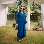 Woman in a blue dress standing outdoors with greenery in the background