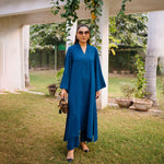 Woman in a blue dress standing outdoors with greenery in the background